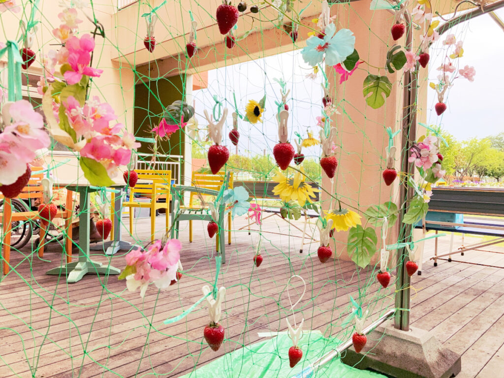 特別養護老人ホーム　ル・リアンふかみの1階ウッドデッキに、ネットと洗濯ばさみで「いちご畑」を設置した写真です。