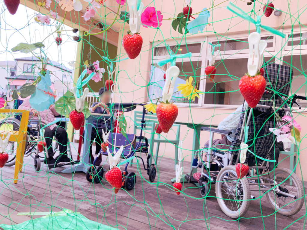 特別養護老人ホーム　ル・リアンふかみの1階ウッドデッキに、ネットと洗濯ばさみで「いちご畑」を設置した写真です。