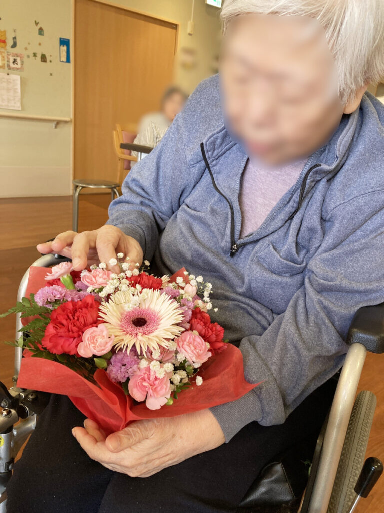特別養護老人ホーム　ル・リアンふかみの「母の日」イベントです。プレゼントの花束を見つめるご利用者様の写真です。