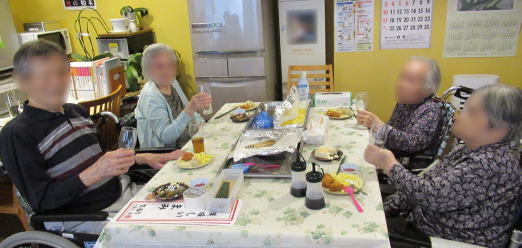 特別養護老人ホーム ル・リアンふかみの1階喫茶室で開催した「ミニ居酒屋レクリエーション」のご様子です。喫茶室のテーブルでグラスを手に、笑顔のご入居者様です。