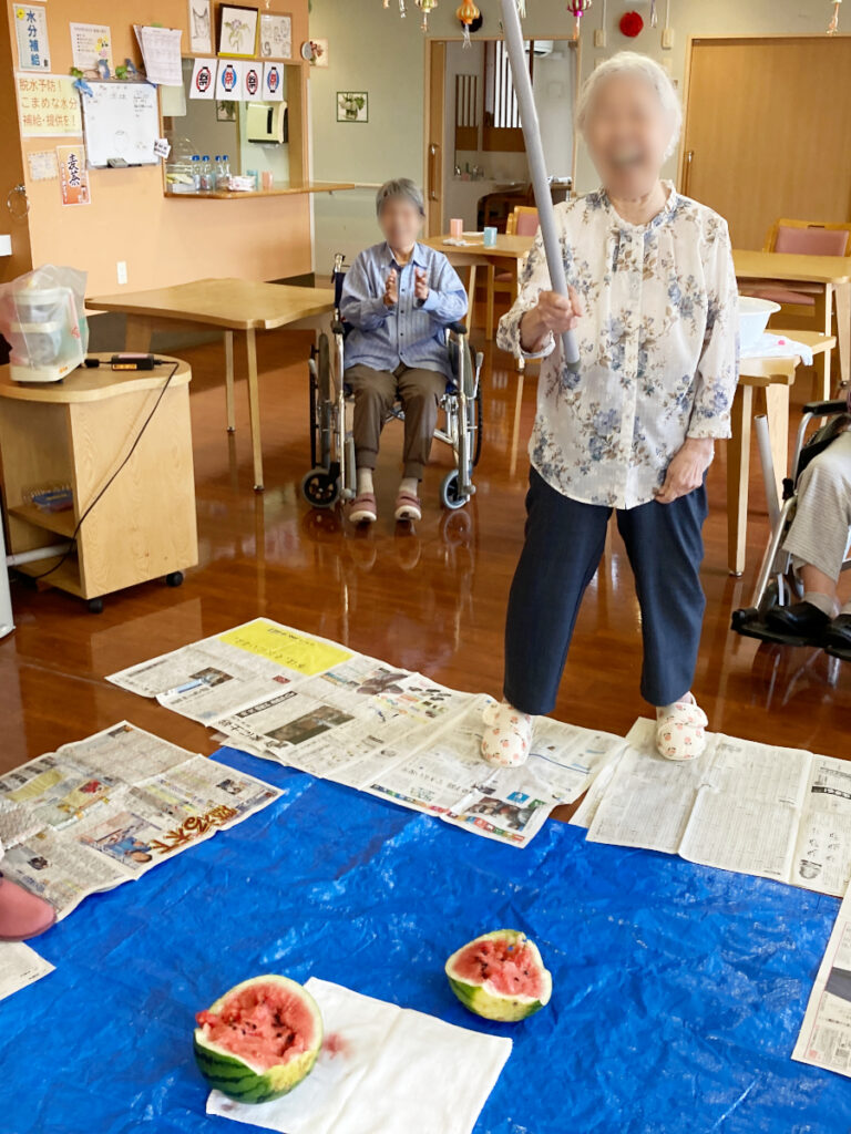 特別養護老人ホーム ル・リアンふかみで開催した「夏祭り」レクリエーションの様子です。スイカ割りを楽しむ、笑顔のご利用者様の写真です。