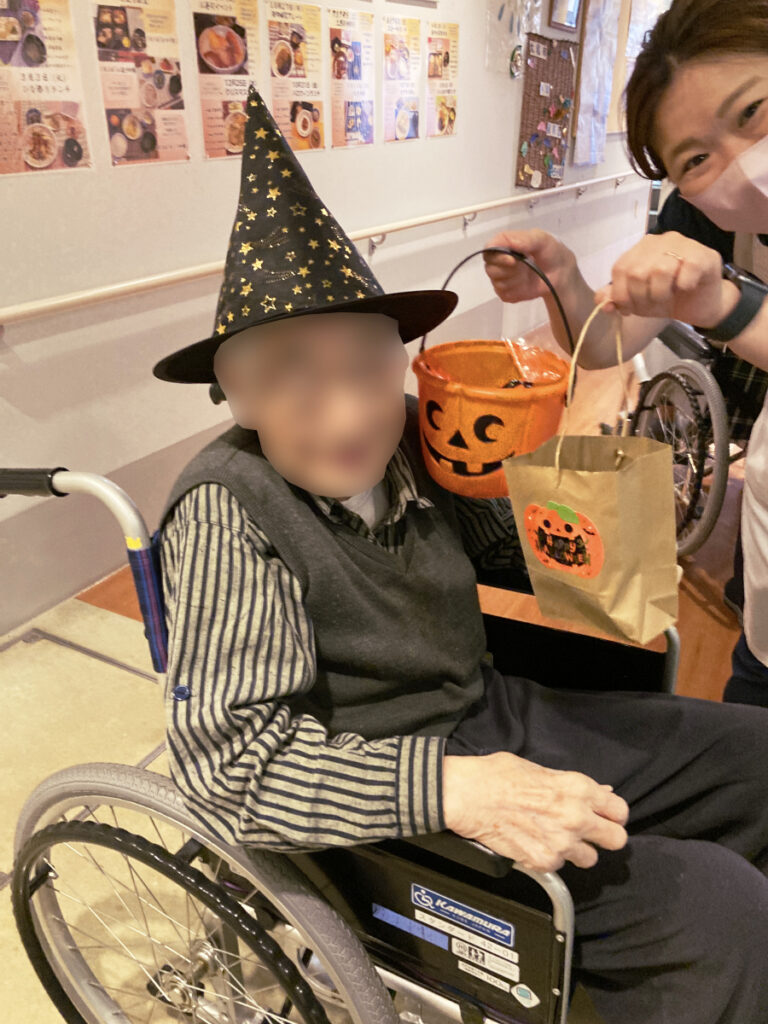 特別養護老人ホーム ル・リアンふかみで、令和8年10月13日(火)に行った「ハロウィンレクリエーション」の様子です。魔法使いの帽子で仮装したご利用者様が、看護師と笑顔で記念撮影!